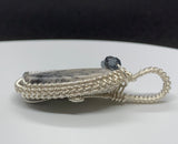 This Burro Creek Agate Pendant is a stunning and unique piece of jewelry, featuring a rare Burro Creek Agate stone with natural dendritic formations resembling trees. Wrapped in high-quality sterling silver (.925) and fine silver (.999), this pendant combines nature’s artistry with expert craftsmanship. The addition of Czech glass accent beads further enhances its beauty, making this pendant a timeless and eye-catching piece.