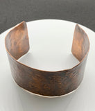This striking wide copper cuff bracelet is hand-embossed with intricate patterns. The rich, warm tones of the copper are enhanced by the detailed embossing, creating a bold yet elegant statement piece.