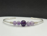 This elegant cuff bracelet is handcrafted from heavy gauge (.925) sterling silver, offering both strength and sophistication. It features a stunning combination of classic Amethyst and striking Dog Tooth Amethyst, showcasing rich purple hues and natural patterning. A powerful statement piece for crystal lovers and those who appreciate artisan silverwork.