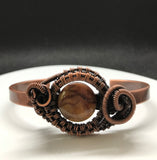 This Hand Woven Copper Cuff Bracelet with Cherry Creek Jasper is a striking piece of jewelry featuring a solid copper cuff with an intricately woven Cherry Creek Jasper centerpiece. This bracelet combines the warmth and durability of copper with the natural beauty of Cherry Creek Jasper, creating a unique and elegant accessory.