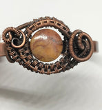 This Hand Woven Copper Cuff Bracelet with Cherry Creek Jasper is a striking piece of jewelry featuring a solid copper cuff with an intricately woven Cherry Creek Jasper centerpiece. This bracelet combines the warmth and durability of copper with the natural beauty of Cherry Creek Jasper, creating a unique and elegant accessory.