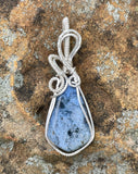 This Beautiful Blue Dumortierite Pendant features a striking blue dumortierite gemstone elegantly encased in wire-wrapped sterling silver. This pendant combines the rich, deep blue tones of dumortierite with the refined sparkle of sterling silver, creating a sophisticated and eye-catching piece of jewelry.