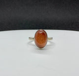 A goldstone glimmers like captured starlight, held in smooth sterling silver — this ring is radiant, refined, and full of warmth.