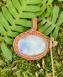 This pendant features a vibrant Rainbow Moonstone with a captivating play of colors. The stone is securely wrapped in intricate handwoven copper, enhancing its natural beauty while adding warmth and elegance.