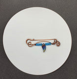 This unique, handcrafted copper pin is made from heavy gauge copper, featuring graceful copper swirls that add texture and movement to the design. The pin is adorned with vibrant blue glass beads and a dazzling rainbow glass leaf accent, bringing a touch of color and whimsy to the piece. Perfect for adding an artistic flair to your outfit, this one-of-a-kind copper pin embodies a blend of rustic elegance and playful charm.