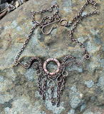 This handcrafted necklace features an embossed copper washer as its centerpiece, accented with wire-wrapped copper details and dangling copper chain.