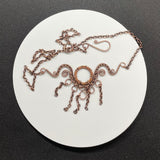 This handcrafted necklace features an embossed copper washer as its centerpiece, accented with wire-wrapped copper details and dangling copper chain.