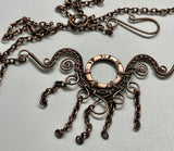 This handcrafted necklace features an embossed copper washer as its centerpiece, accented with wire-wrapped copper details and dangling copper chain.
