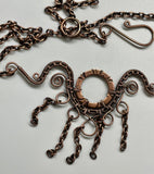 This handcrafted necklace features an embossed copper washer as its centerpiece, accented with wire-wrapped copper details and dangling copper chain.