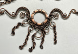 This handcrafted necklace features an embossed copper washer as its centerpiece, accented with wire-wrapped copper details and dangling copper chain.