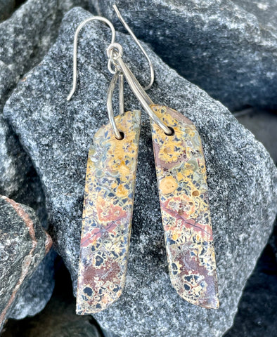 Embrace earthy elegance with these earrings that feature Leopard Skin Jasper stones suspended from sterling silver triangles. The unique patterns of the jasper resemble nature's artistry, creating a truly one-of-a-kind design. Paired with sleek sterling silver ear wires, these earrings offer a perfect balance of rustic charm and modern sophistication. 