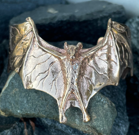 This unique bangle bracelet features a striking bat motif, crafted in warm, hand-forged copper. The intricate design captures the bat’s wings in mid-flight, adding a touch of mystery and intrigue to this piece. Perfect for those who appreciate nature-inspired jewelry with a hint of gothic flair, this bangle makes a bold and memorable statement.