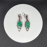 These handcrafted earrings feature rich green malachite stones wrapped in a combination of square and twisted square copper wire, adding depth and dimension to the design. The swirling bands of the malachite beautifully complement the warm copper tones, while hypoallergenic niobium ear wires ensure all-day comfort. A perfect blend of bold elegance and natural beauty—ideal for everyday wear or special occasions.