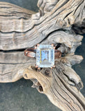 This enchanting ring features a large, faceted clear quartz gemstone that sparkles with natural brilliance. Set in warm copper, the band is adorned with delicate leaf and flower motifs, adding a touch of botanical elegance to the bold, eye-catching design.