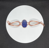 This bracelet features a richly colored carved Lapis Lazuli centerpiece, etched in a criss-cross pattern that adds eye-catching shine and texture. Set in warm copper wire, the design blends bold color with rustic elegance. The adjustable fit ensures comfort and versatility, making this a striking accessory for any wrist.
