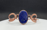 This bracelet features a richly colored carved Lapis Lazuli centerpiece, etched in a criss-cross pattern that adds eye-catching shine and texture. Set in warm copper wire, the design blends bold color with rustic elegance. The adjustable fit ensures comfort and versatility, making this a striking accessory for any wrist.