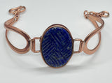 This bracelet features a richly colored carved Lapis Lazuli centerpiece, etched in a criss-cross pattern that adds eye-catching shine and texture. Set in warm copper wire, the design blends bold color with rustic elegance. The adjustable fit ensures comfort and versatility, making this a striking accessory for any wrist.