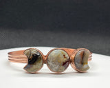 This celestial-inspired copper bangle features two Laguna Lace Agate crescent moons and one striking full moon centerpiece. The natural swirls and vibrant banding of the agate stones create a beautiful contrast against the copper setting. A symbolic and one-of-a-kind bracelet that captures the magic of moon phases.