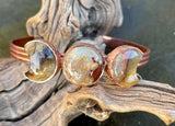 This celestial-inspired copper bangle features two Laguna Lace Agate crescent moons and one striking full moon centerpiece. The natural swirls and vibrant banding of the agate stones create a beautiful contrast against the copper setting. A symbolic and one-of-a-kind bracelet that captures the magic of moon phases.