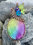 This vibrant pendant features a stunning dyed Rainbow Quartz centerpiece, showcasing a spectrum of colors that beautifully catch the light. Wrapped in warm copper, the pendant is adorned with delicate glass flowers and a charming leaf accent, adding an artistic touch to the design. This unique piece celebrates the beauty of nature and color, making it a perfect statement accessory for any outfit. Whether for everyday wear or special occasions, this pendant is sure to brighten your jewelry collection!