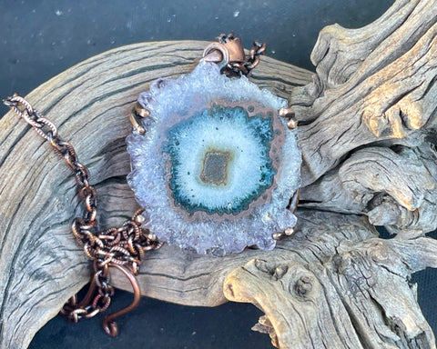 This Purple, Brown, Green, and White Stalactite Slice Necklace features a beautifully natural stalactite slice adorned with a variety of colors including purple, brown, green, and white, all set in copper. This necklace highlights the unique geological beauty of stalactites and the artisanal craftsmanship of copper jewelry.