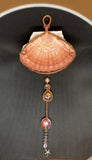 This Large Irish Flat Scallop Shell Sun Catcher features a beautifully natural Irish flat scallop shell adorned with woven copper wire, glass beads, crystals, and a starfish dangle. This sun catcher is designed to capture and reflect light, creating a shimmering and decorative effect.