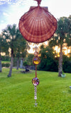 This Large Irish Flat Scallop Shell Sun Catcher features a beautifully natural Irish flat scallop shell adorned with woven copper wire, glass beads, crystals, and a starfish dangle. This sun catcher is designed to capture and reflect light, creating a shimmering and decorative effect.