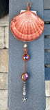 This Large Irish Flat Scallop Shell Sun Catcher features a beautifully natural Irish flat scallop shell adorned with woven copper wire, glass beads, crystals, and a starfish dangle. This sun catcher is designed to capture and reflect light, creating a shimmering and decorative effect.