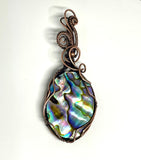 This Abalone Doublet Pendant features a stunning abalone shell layered in a doublet style, framed in handwoven copper. The vibrant, iridescent hues of the abalone shell—ranging from deep blues to greens and purples—contrast beautifully with the warmth of the copper. The doublet construction enhances the natural colors of the abalone, making this pendant an eye-catching piece that brings the beauty of the ocean to life.