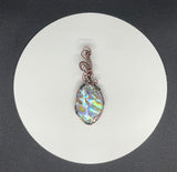 This Abalone Doublet Pendant features a stunning abalone shell layered in a doublet style, framed in handwoven copper. The vibrant, iridescent hues of the abalone shell—ranging from deep blues to greens and purples—contrast beautifully with the warmth of the copper. The doublet construction enhances the natural colors of the abalone, making this pendant an eye-catching piece that brings the beauty of the ocean to life.