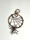 This unique and spooky pendant features an intricately handcrafted copper spider web, complete with a dangling copper spider. The spider is adorned with a luminous Mother of Pearl bead, adding a touch of elegance to the eerie design. Perfect for those who love nature-inspired or Halloween-themed jewelry, this pendant blends whimsy with artistic craftsmanship, making it a standout piece for any occasion.