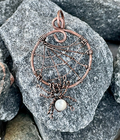 This unique and spooky pendant features an intricately handcrafted copper spider web, complete with a dangling copper spider. The spider is adorned with a luminous Mother of Pearl bead, adding a touch of elegance to the eerie design. Perfect for those who love nature-inspired or Halloween-themed jewelry, this pendant blends whimsy with artistic craftsmanship, making it a standout piece for any occasion.