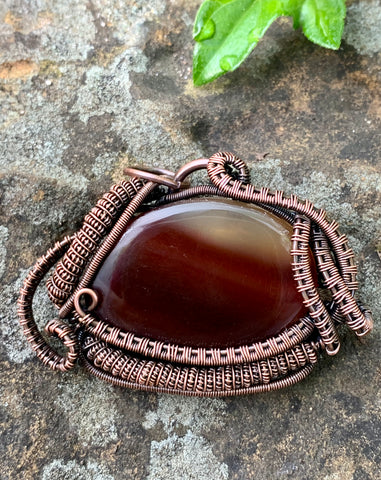 This pendant has a richly colored Agate with shades of chocolate, coffee to clear, wrapped in layers of handwoven and hand coiled copper.