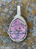 This exquisite pendant features a stunning rose-colored Rhodonite cabochon, characterized by striking black lines that create a unique and captivating design. Expertly wrapped in handwoven sterling silver (.925) and fine silver (.999), the pendant showcases exceptional craftsmanship and elegance. The soft hues of the Rhodonite combined with the lustrous silver create a beautiful contrast, making this piece a perfect addition to any jewelry collection. 