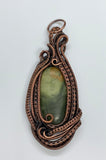 This pendant has swirling layers of handwoven copper surround this multi-colored green Serpentine.