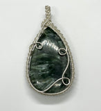 This breathtaking pendant showcases a large Seraphinite gemstone, renowned for its deep green color and feather-like patterns. The stone is intricately wrapped in Argentium Silver, known for its brilliance and tarnish resistance, creating an elegant contrast that highlights the natural beauty of the Seraphinite. Perfect for those who appreciate unique, nature-inspired jewelry, this pendant is a timeless statement piece with a graceful and ethereal charm.