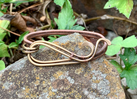 This standout bracelet features hammered brass waves, interwoven with intricate handwoven copper detailing. The combination of textures and warm metallic tones creates a unique and eye-catching piece that exudes both elegance and craftsmanship. Perfect for those who love bold, artisanal jewelry, this bracelet adds a touch of sophistication to any look.