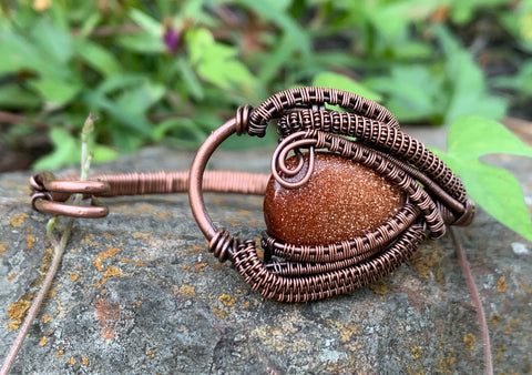 Heavy gauge Copper forms the base of this bracelet with a shimmering Goldstone Cabochon caught in the copper weaves. 