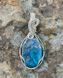 This exquisite pendant showcases a striking blend of deep blue Shattuckite and shimmering metallic Tenorite, elegantly wrapped in Argentium silver wire. The intricate wirework enhances the stone’s natural beauty while providing a sleek, modern touch. With its rich hues and artisan craftsmanship, this unique pendant is a perfect statement piece for those who appreciate rare gemstones and handcrafted elegance.