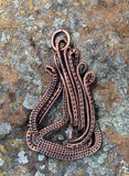 This Pendant features asymmetrical layers of hand wrapped, woven and coiled copper wire with a quartz bead accent.