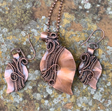 This stunning set features hand-cut, formed, and textured solid copper leaves, expertly wrapped with intricately woven copper. The pendant and matching earrings showcase the beauty of artisanal craftsmanship, capturing the organic elegance of nature. The rich, warm tones of the copper create a harmonious and versatile look, perfect for adding a touch of rustic charm to any outfit. This unique set makes a thoughtful gift for nature lovers or a beautiful addition to your own jewelry collection.