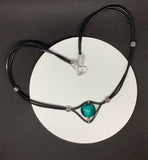 This charming necklace features a beautifully crafted teal-colored Lampwork glass bead as its centerpiece. The unique patterns within the glass add depth and intrigue, making it a standout piece. The bead is strung on supple leather, adding a rustic yet elegant touch. Perfect for layering or wearing on its own, this necklace is a versatile addition to any jewelry collection.