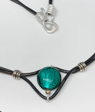 This charming necklace features a beautifully crafted teal-colored Lampwork glass bead as its centerpiece. The unique patterns within the glass add depth and intrigue, making it a standout piece. The bead is strung on supple leather, adding a rustic yet elegant touch. Perfect for layering or wearing on its own, this necklace is a versatile addition to any jewelry collection.