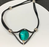 This charming necklace features a beautifully crafted teal-colored Lampwork glass bead as its centerpiece. The unique patterns within the glass add depth and intrigue, making it a standout piece. The bead is strung on supple leather, adding a rustic yet elegant touch. Perfect for layering or wearing on its own, this necklace is a versatile addition to any jewelry collection.