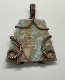 Make a bold statement with this stunning wire-wrapped pendant featuring a large lazulite gemstone in soft hues of light blue and tan. Expertly handcrafted with warm copper wire, this piece highlights the natural beauty of lazulite's intricate patterns. The rich copper tones perfectly complement the stone’s serene colors, creating a timeless accessory that's ideal for nature lovers and bohemian styles alike.