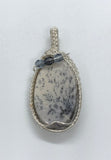 This Burro Creek Agate Pendant is a stunning and unique piece of jewelry, featuring a rare Burro Creek Agate stone with natural dendritic formations resembling trees. Wrapped in high-quality sterling silver (.925) and fine silver (.999), this pendant combines nature’s artistry with expert craftsmanship. The addition of Czech glass accent beads further enhances its beauty, making this pendant a timeless and eye-catching piece.