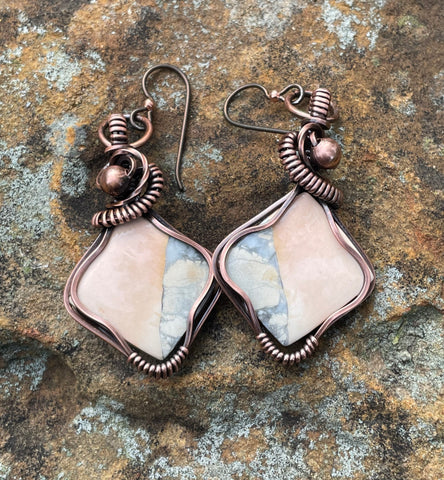 These Delightful Peach and Gray Maligano Jasper Earrings are a unique and striking combination of natural beauty and artisan craftsmanship. Featuring beautiful peach and gray Maligano Jasper stones, these earrings are wrapped in copper wire for an earthy yet elegant look. Paired with hypoallergenic niobium ear wires, these earrings are both stylish and comfortable, perfect for those with sensitive skin.