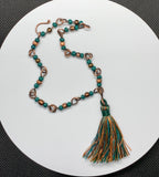 Alternating colored glass beads in copper anklet with a silk 1 3/4" tassel. 
