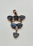 This Copper Pendant featuring 6 Blue Dumortierite Cabochons and 3 Faceted Rainbow Moonstones is a striking and intricate piece of jewelry. The pendant showcases a sophisticated blend of blue dumortierite and rainbow moonstone, all elegantly set in copper. This pendant embodies a harmonious combination of deep, rich colors and vibrant, iridescent highlights.