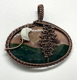 This Ocean Jasper Pendant is a beautifully handcrafted jewelry piece wrapped in Copper, featuring a striking Tree design alongside a delicate Moon accent. The pendant's centerpiece is a naturally vibrant Ocean Jasper stone, showcasing a range of earthy tones that resemble the serene beauty of nature.